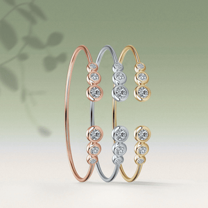 Three diamond-studded bangles in rose gold, silver, and yellow gold on a light green background.
