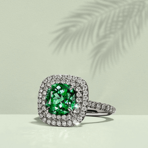 Ring with a green gemstone and diamond halo on a light background