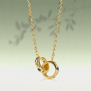 Gold necklace with interlocking rings and blue stones on a light green background