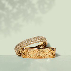 Two gold rings with intricate designs on a light green background