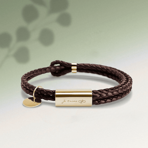 Brown braided leather bracelet with gold tag on a light green background