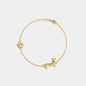 Gold chain bracelet featuring a dachshund dog charm and a small paw print accent, secured with a lobster clasp, displayed on a white background.