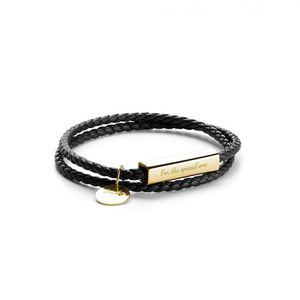 Black braided leather bracelet with gold tag and heart charm on a white background