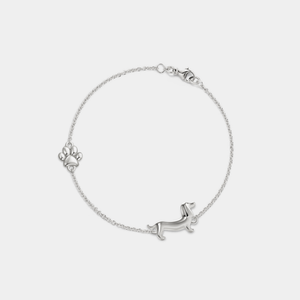 Silver chain bracelet featuring a dachshund dog charm and a small paw print accent, secured with a lobster clasp, displayed on a white background.