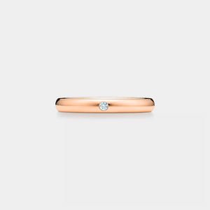 Rose gold ring with a small moissanite on a light gray background
