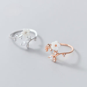 Two floral-themed rings, one silver and one rose gold, on a light gray background.