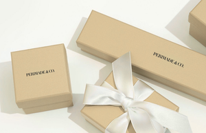 Two beige gift boxes with white ribbons on a light background, featuring the brand 'Permade & Co'.