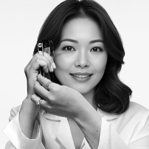 Black and white photo of a woman holding holding gemstone tweezers up to her eye, displaying diamonds.