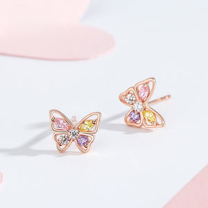 Butterfly-shaped earrings with colorful gemstones on a light pink background