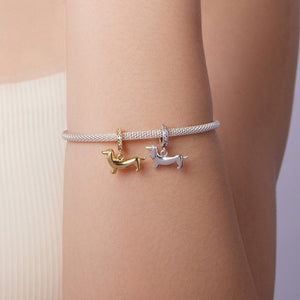 A bracelet with two dachshund charms on a wrist against a neutral background