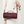 Maroon handbag with gold accents held by a person wearing a white coat.