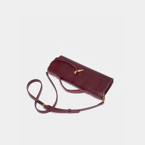 Maroon handbag with a strap on a light gray background