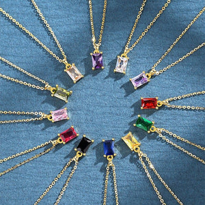 A collection of baguette cut birthstone pendant necklaces in various colors, set in gold plating, displayed on a blue background.