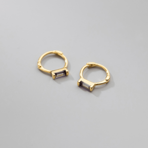Gold hoop earrings with purple gemstones on a gray background