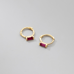 Gold hoop earrings with red gemstones on a gray background