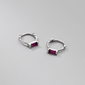 Silver hoop earrings with red gemstones on a light gray background