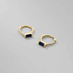 Gold hoop earrings with blue gemstones on a gray background