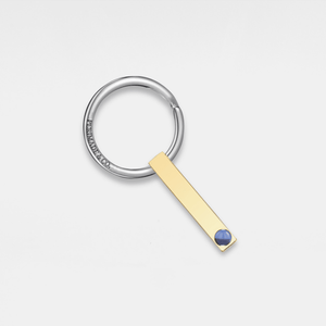 Gold keychain with a blue gemstone on a light gray background