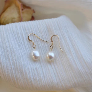 A set of three baroque pearl dangle drop earrings with gold plating, displayed on a white surface with a dried flower and part of a white garment visible in the background.