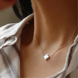 Close-up of a gold necklace with a white pendant worn by a person.