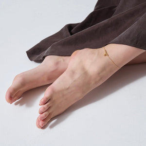 Feet with a gold anklet on a light gray background