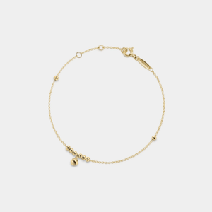 Gold bracelet with small beads on a light gray background