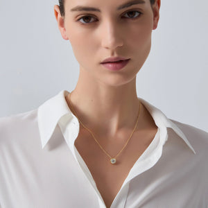 Woman wearing a gold necklace with a white shirt on a plain background