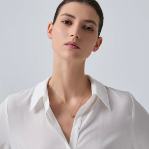 Woman wearing a white shirt and a delicate necklace on a light gray background