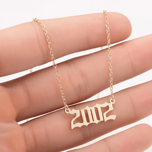 Gold necklace with '2012' pendant held between fingers on a white background