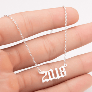 Silver necklace with '2018' pendant held between fingers on a white background