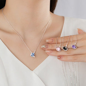 Necklace with heart-shaped pendant and three additional pendants on a hand against a neutral background