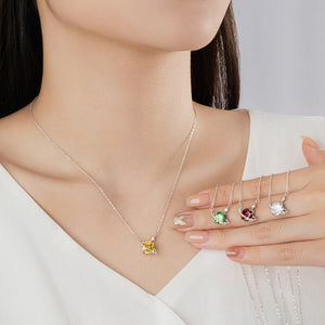Woman wearing a silver necklace with a yellow gemstone, holding three additional necklaces with different gemstones.