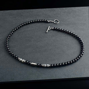 Three black agate crystal bead necklaces with varying details, displayed on a grey surface. One necklace features gold plating, another has a smooth finish, and the third includes metallic bead accents.