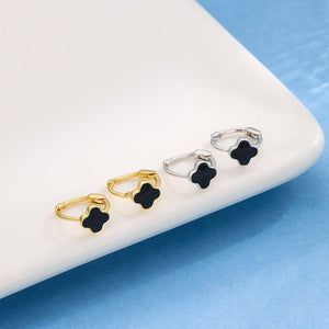 Four black clover-shaped earrings on a white surface with a blue background