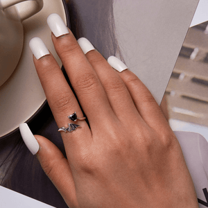 Hand with white nail polish wearing two rings, blurred background