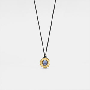 Gold pendant with a blue stone on a black cord against a light gray background