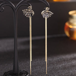 Pair of long, thin earrings with decorative tops on a black stand.