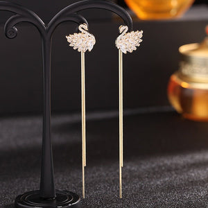Swan-shaped earrings on a black stand with a blurred background