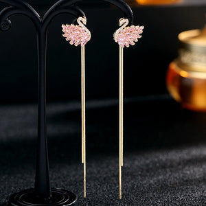 Pink swan earrings on a black stand with a blurred background