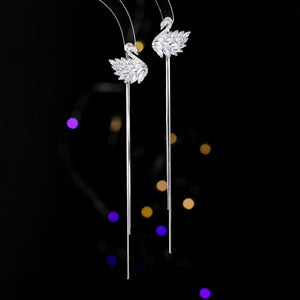 Silver swan-shaped earrings on a black background with colorful bokeh lights.