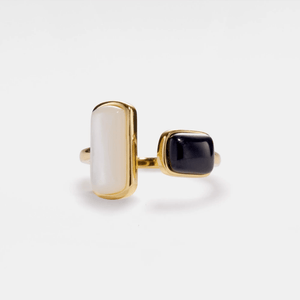 Gold ring with a white stone and black gemstone on a light gray background