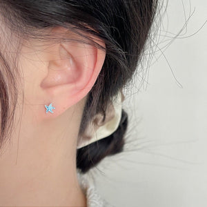 Close-up of an ear wearing a blue starfish-shaped earring with a neutral background