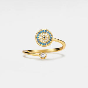 Gold evil eye spinner ring with blue gemstones and a black center gemstone on a light gray background