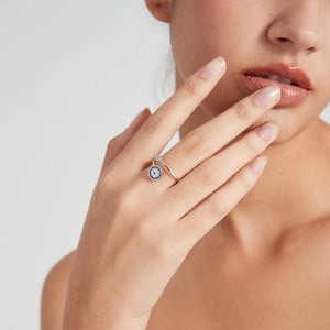 Close-up of a hand wearing a silver evil eye spinner ring with a blue gemstone on a neutral background