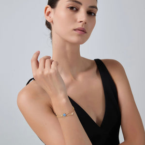 Woman wearing a gold bracelet with colorful stones on a plain background