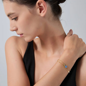 Woman wearing a gold bracelet with a blue gemstone on a plain background