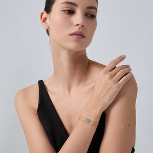 Woman wearing a black dress and gold bracelet with a blue gemstone on a gray background