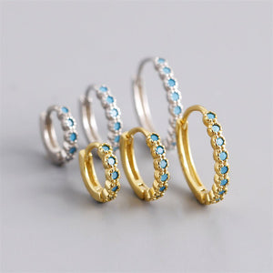 Gold and silver hoop earrings with blue gemstones on a light gray background