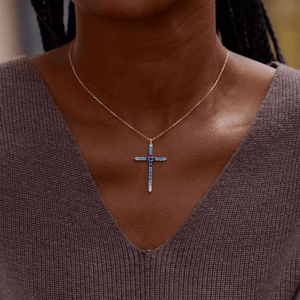 Necklace with a cross pendant featuring blue and clear stones on a person wearing a brown sweater.