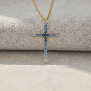 Gold cross necklace with blue gemstones on a textured surface